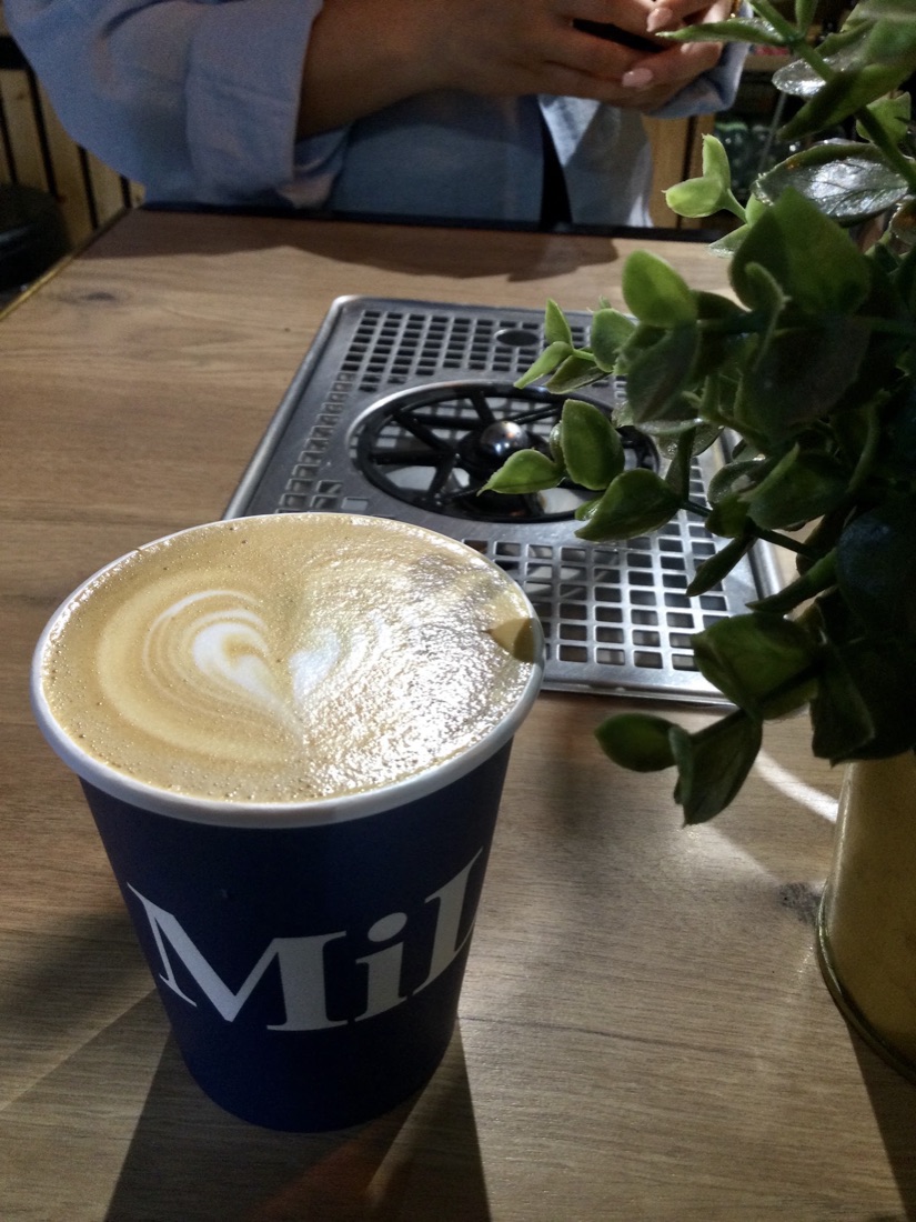 A Milk branded navy takeaway cup with a fresh coffee