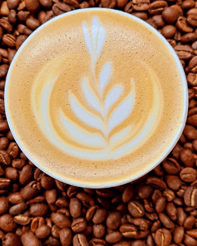 Rosetta latte art on a bed of coffee beans